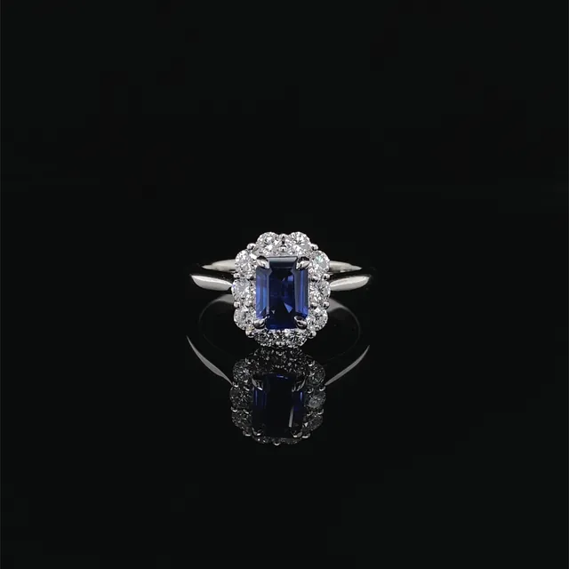 An emerald cut blue stone ring with a diamond halo on black