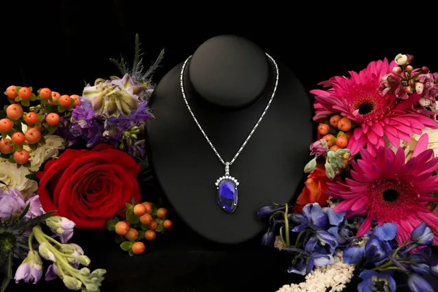 A deep blue oval halo pendant on a black bust with flowers