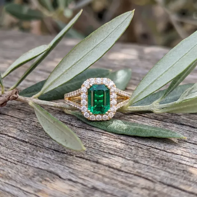 A yellow gold emerald halo ring on an olive branch