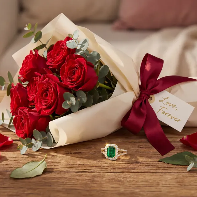 An emerald ring beside a bouquet of red roses