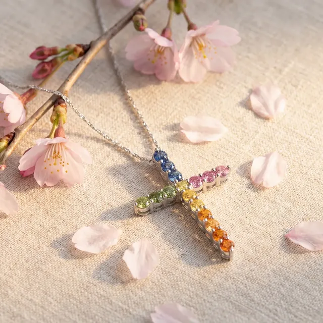 A yellow gold cross set with rainbow colored stones among blossoms