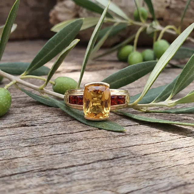 A yellow gold ring with a golden cushion stone on an olive branch