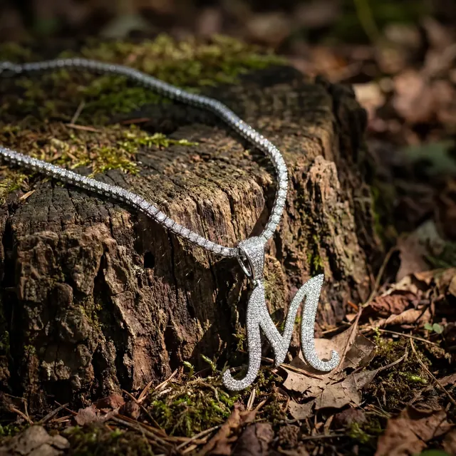 A diamond script initial pendant on a tree stump