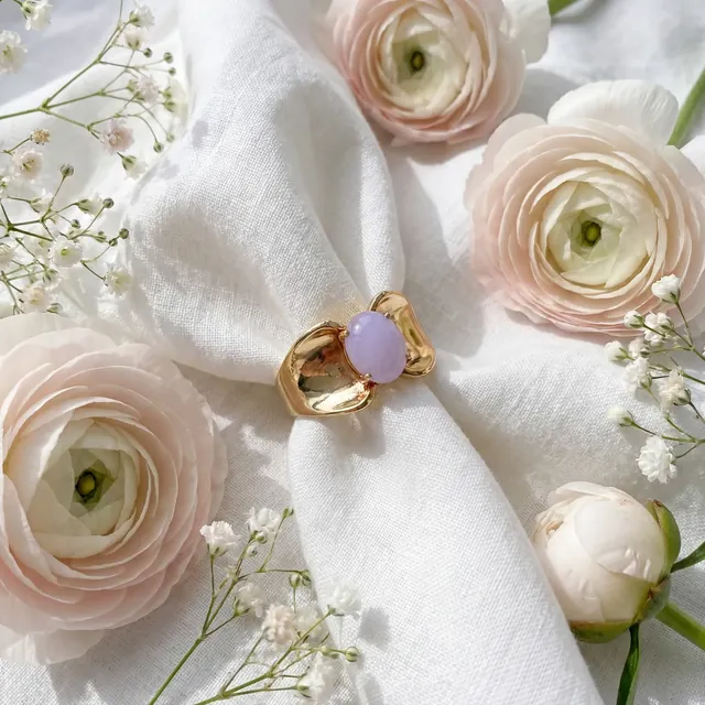 A yellow gold ring with a lavender oval stone among ranunculus flowers