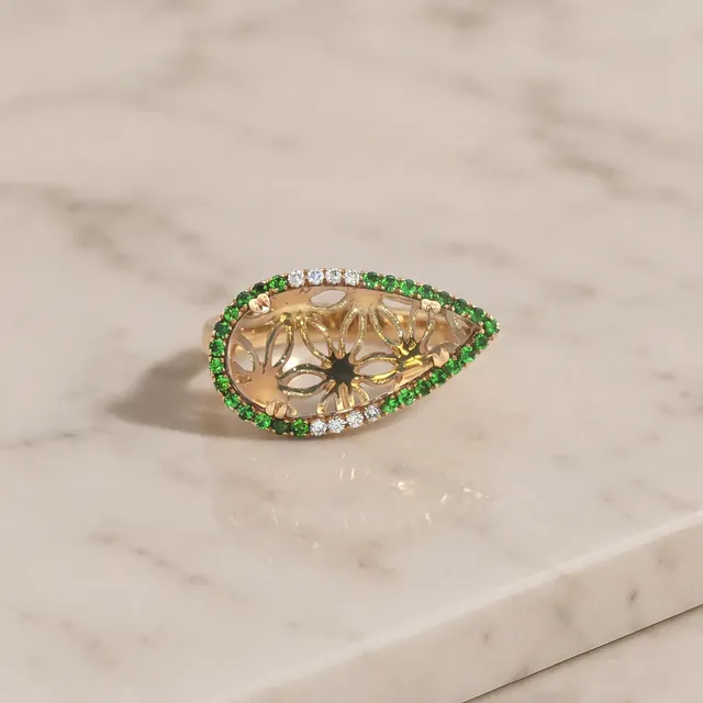 A yellow gold navette ring bordered with green stones on marble