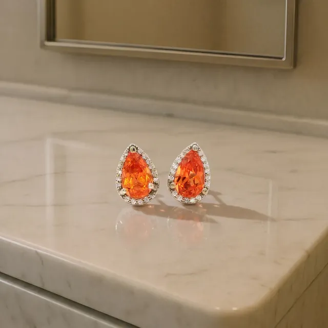 Orange pear stone earrings with diamond halos on marble
