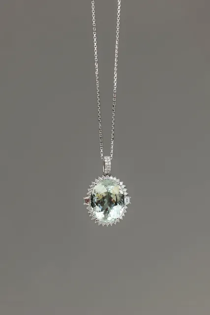 A pale blue green oval stone pendant with a diamond bail on a white gold chain