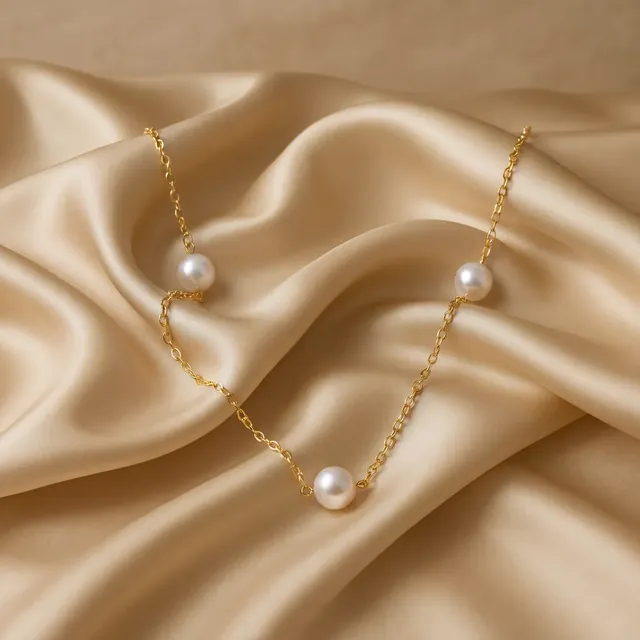 A gold chain with pearls spaced along it on cream satin
