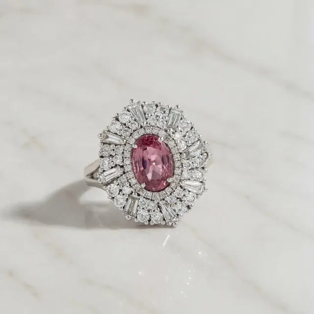 A pink oval stone in a starburst of diamonds on marble