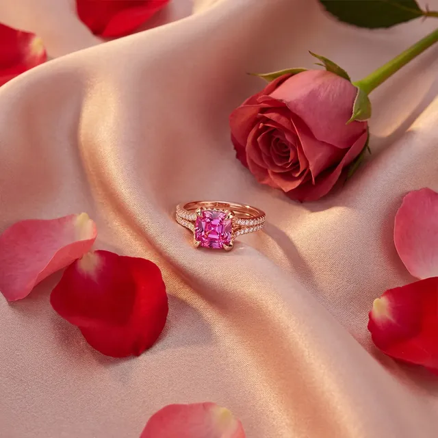 A rose gold ring with a pink stone on pink silk with rose petals