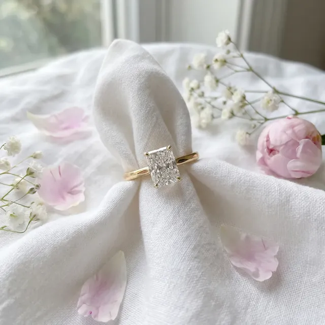 A yellow gold radiant diamond ring resting on white linen