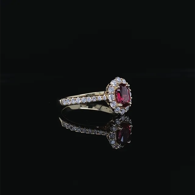 A red oval stone ring with a diamond halo and pave band in yellow gold