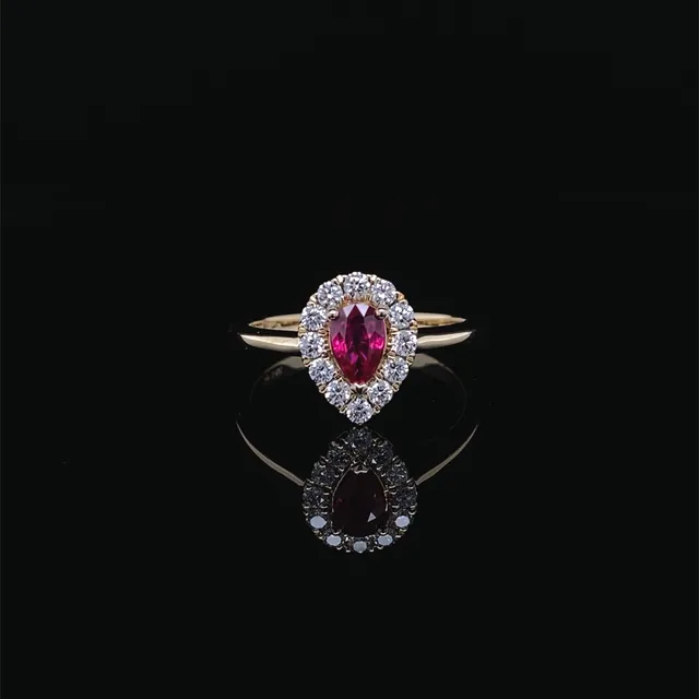 A red pear shaped stone ring with a diamond halo in yellow gold