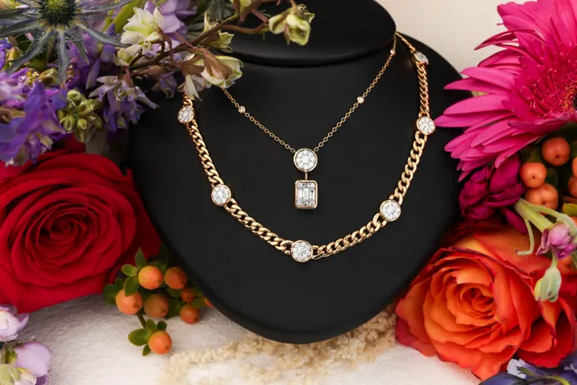 Two rose gold necklaces on a black bust among red, orange and pink flowers