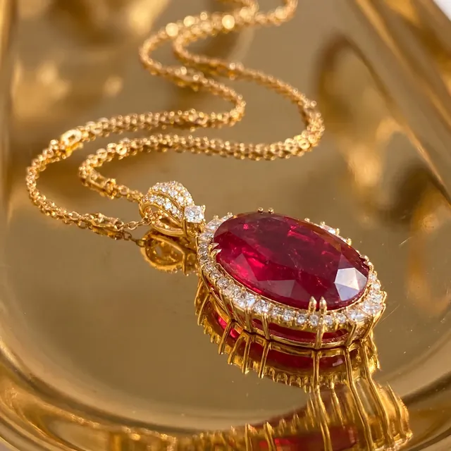A ruby and diamond pendant on a gold tray